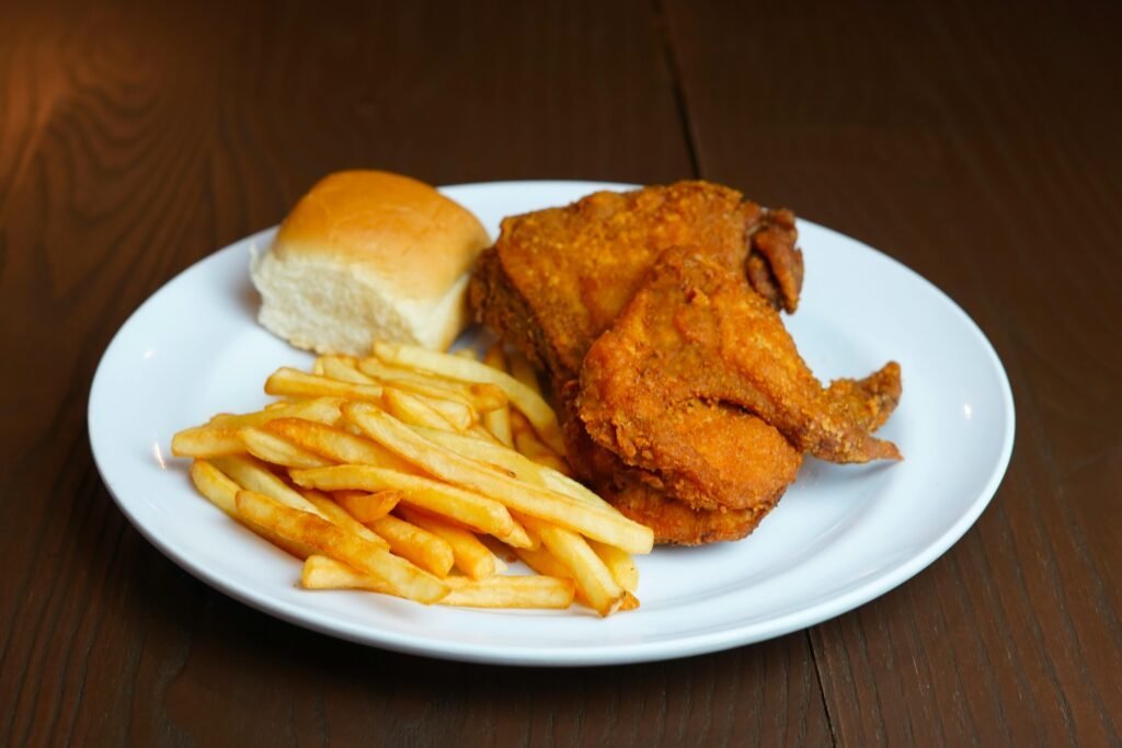Delicious fried chicken served with crispy French fries and a roll on a white plate.