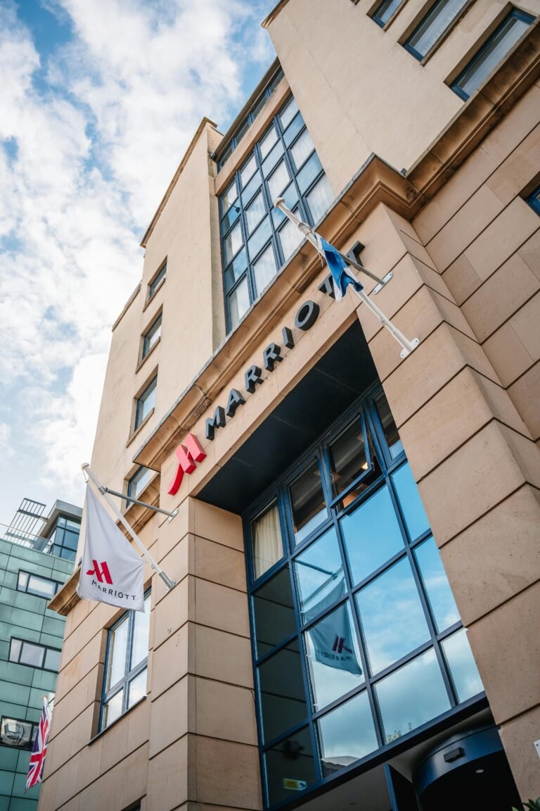 Upward view of a modern Marriott hotel facade under a clear blue sky.