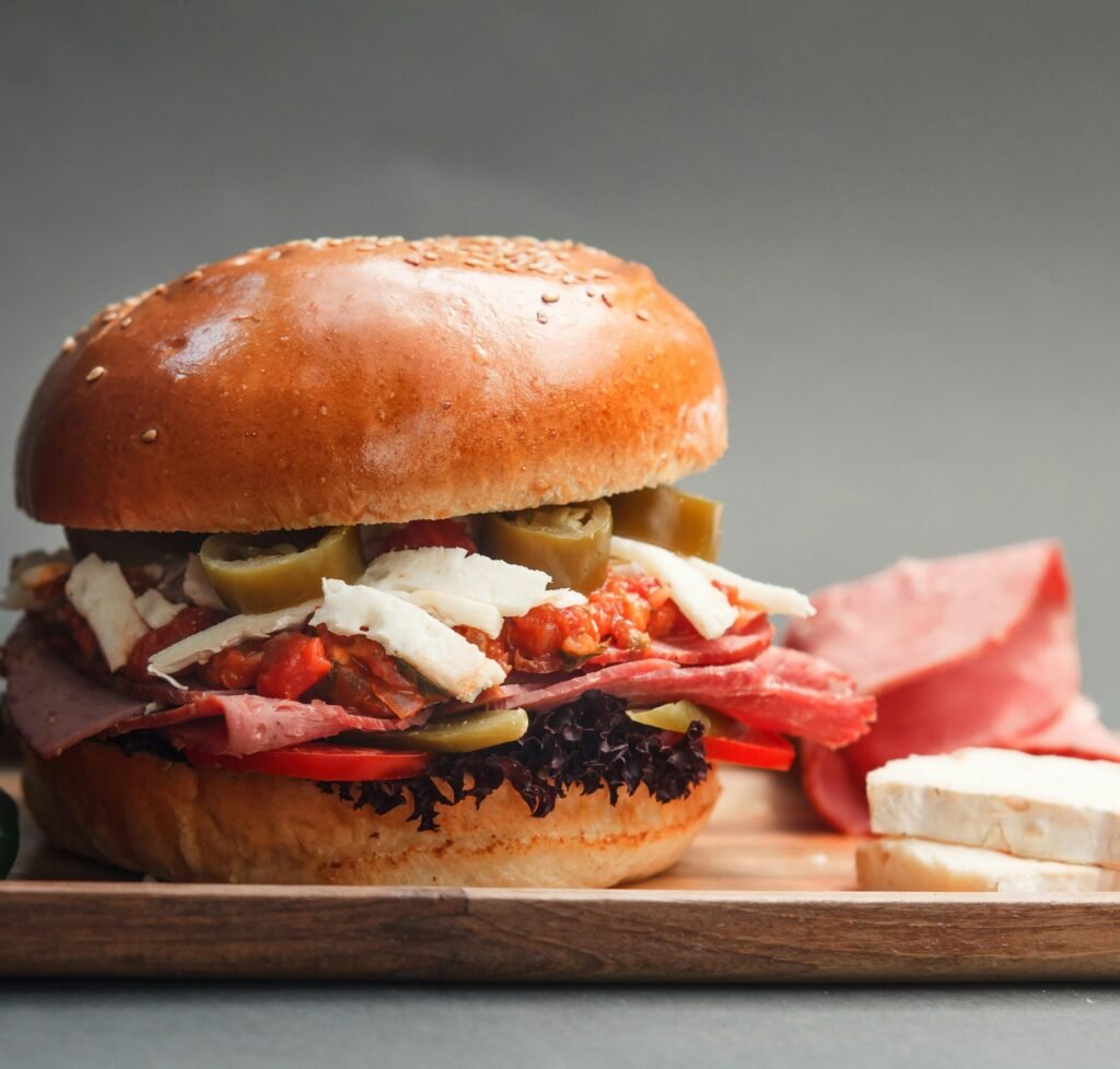 Close-up of a gourmet sandwich with cheese, ham, and vegetables on a cutting board.